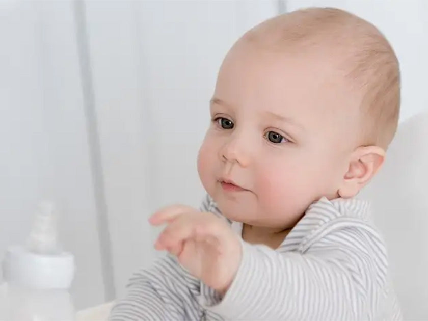 Portrait d’un bébé en vêtements rayés, regardant attentivement quelque chose hors champ, avec un biberon flou en arrière-plan.