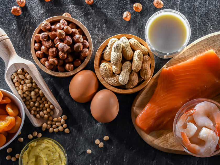 Divers aliments allergènes courants présentés sur une table : noisettes, arachides, œufs, lait, saumon, crevettes, lentilles, abricots secs et purée d'avocat