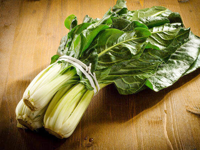 Un bouquet de blettes fraîches avec des feuilles vertes et des côtes blanches, posé sur une table en bois.