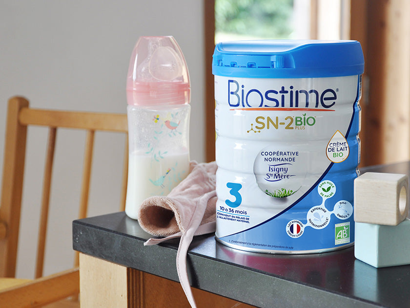 Boîte de lait infantile Biostime SN-2 Bio posée sur une table, à côté d’un biberon rempli de lait
