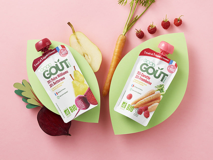 Deux gourdes alimentaires pour bébés de la marque "Good Goût", posées sur un fond rose avec des fruits et légumes frais en décoration, dont poire, betterave, carotte et cerises.