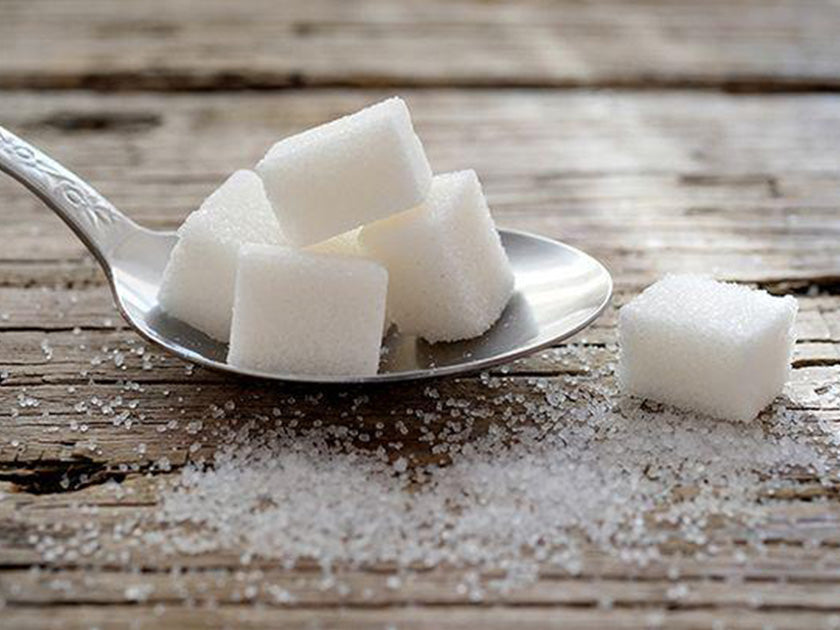 Une cuillère en métal contenant plusieurs morceaux de sucre en cube, posée sur une table en bois avec des grains de sucre éparpillés autour.