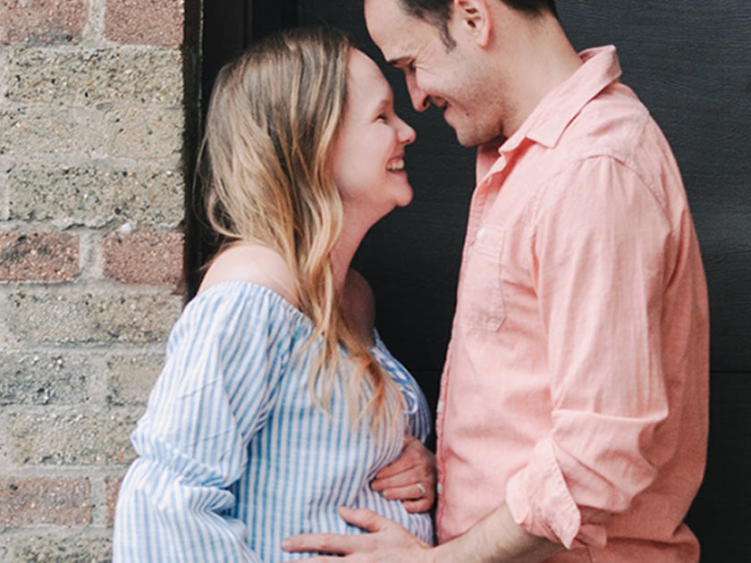 Couple souriant se regardant tendrement, la femme enceinte posant ses mains sur son ventre.  