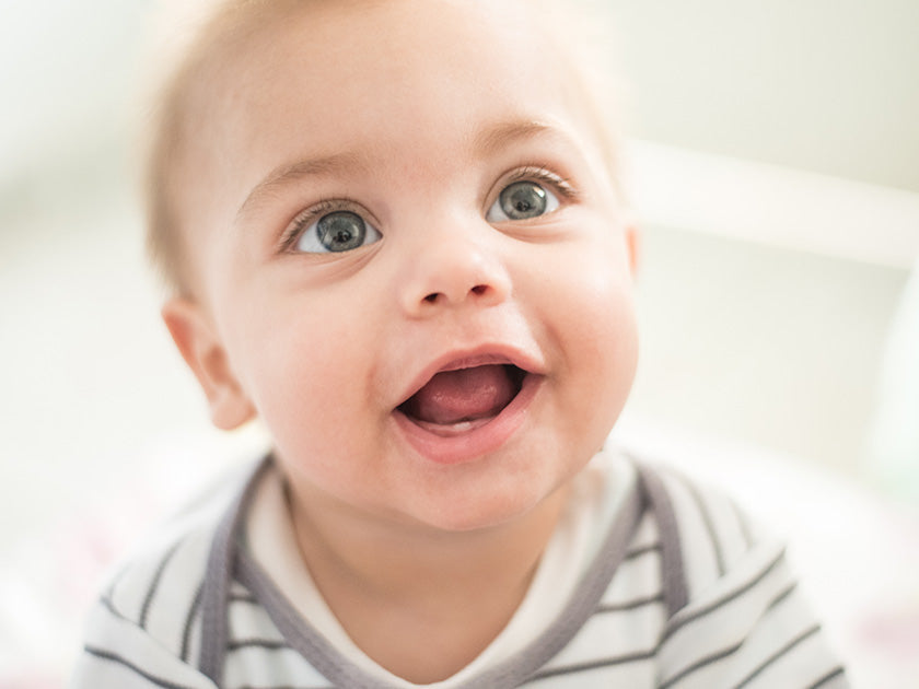 Bébé souriant, regard lumineux et bouche ouverte, habillé d’un body rayé, capturé dans un moment joyeux et naturel en intérieur.