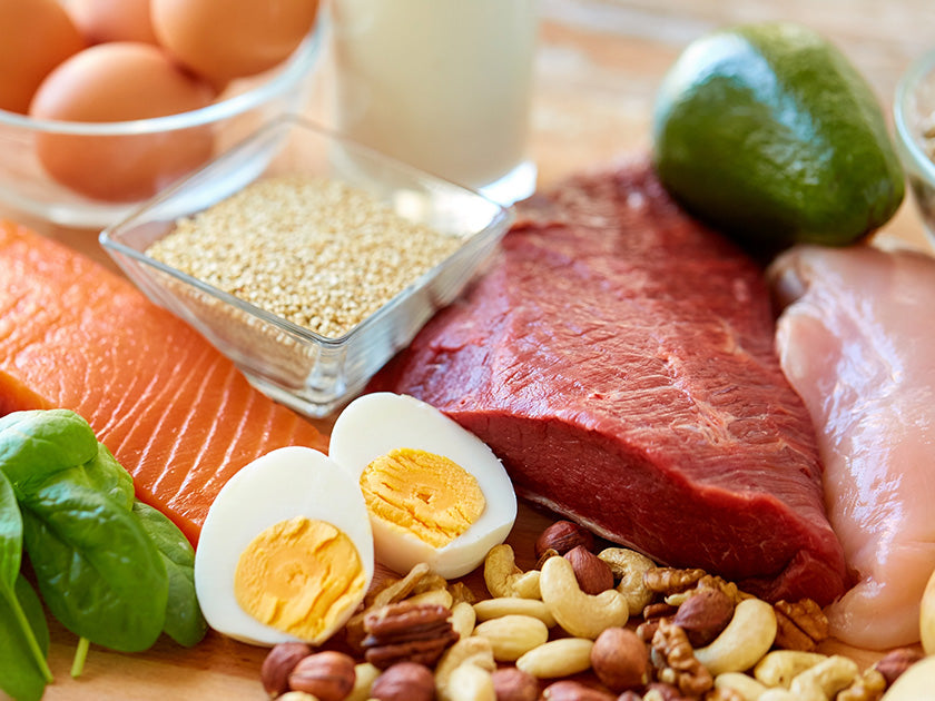 Assortiment d’aliments riches en protéines, incluant du saumon, de la viande rouge, du poulet, des œufs, des noix, du quinoa, des épinards, un avocat et un verre de lait.