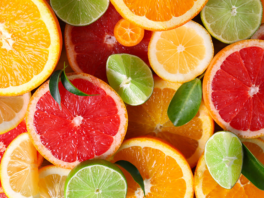 Tranches colorées d’agrumes variés, dont pamplemousses, citrons, citrons verts et oranges, disposées de manière esthétique avec quelques feuilles vertes.