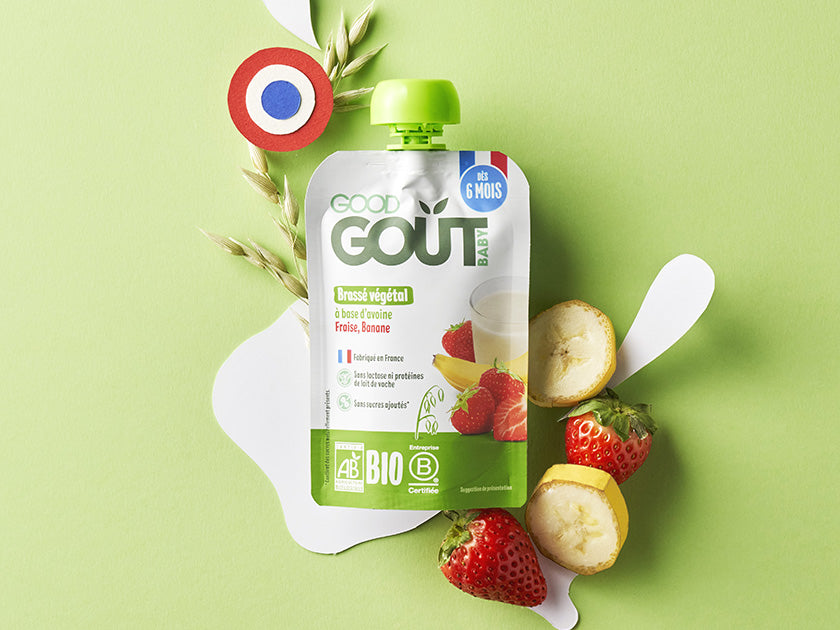 Gourde alimentaire pour bébé de la marque "Good Goût" posée sur un fond vert, accompagnée de fraises, rondelles de banane et de céréales. Un petit drapeau français est visible, mettant en avant l'origine du produit