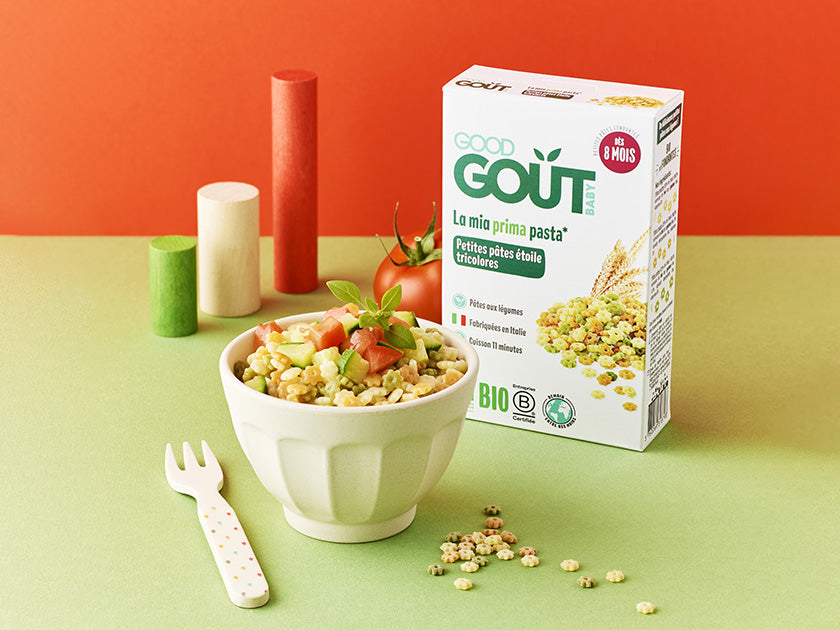 Packaging de céréales bio « Good Goût » avec un bol de céréales garnies de petits morceaux de tomates, une petite fourchette à pois à côté, le tout posé sur une surface verte avec un fond orange.