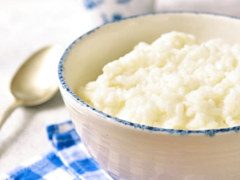 Riz au lait crémeux, posé sur une serviette à carreaux bleus et blancs, avec une cuillère en arrière-plan. 