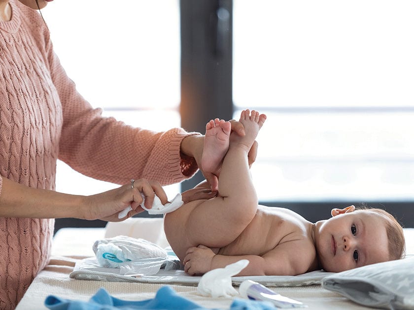 Bébé allongé sur une table à langer pendant qu'une personne lui change la couche.